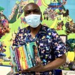Dr Remy Toko smiling at the Paediatric wards holding a handful of children's books.